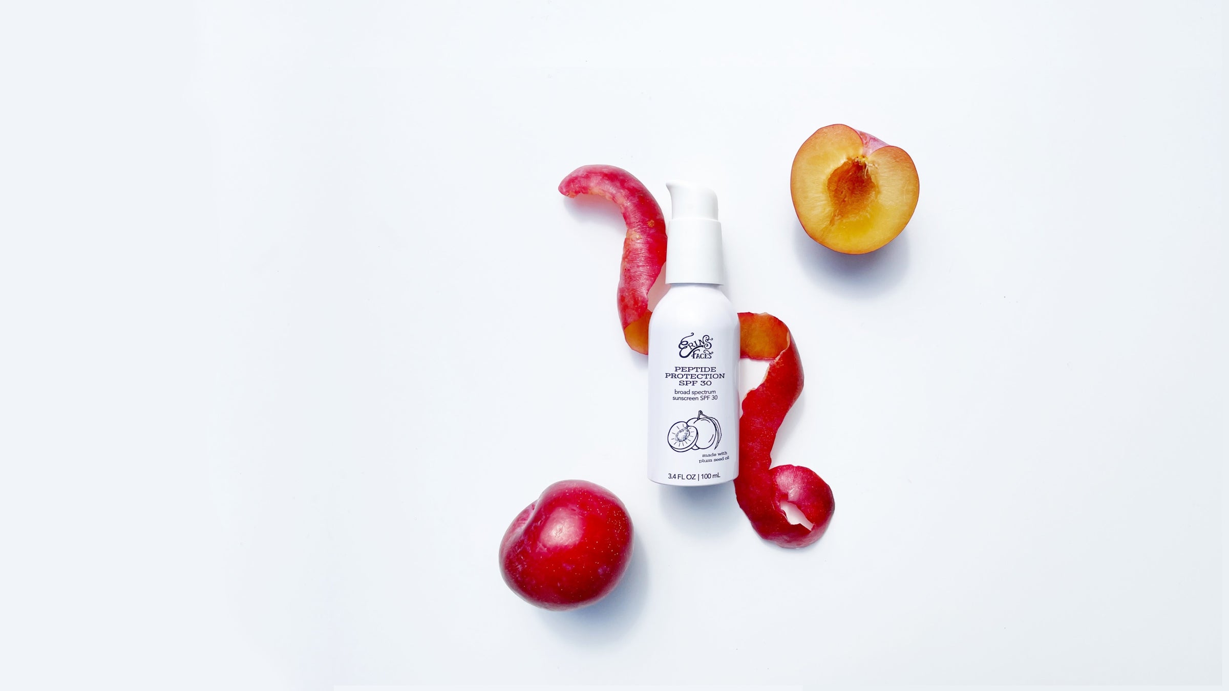 WHITE SPF BOTTLE ON WHITE BACKGROUND WITH RED PLUMS