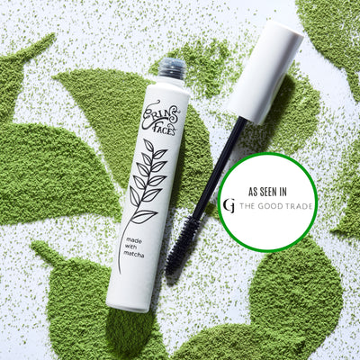 erin's faces matcha mascara white tube with black writing laying on white background with green leaves made of matcha powder + "as seen in the good trade" 
