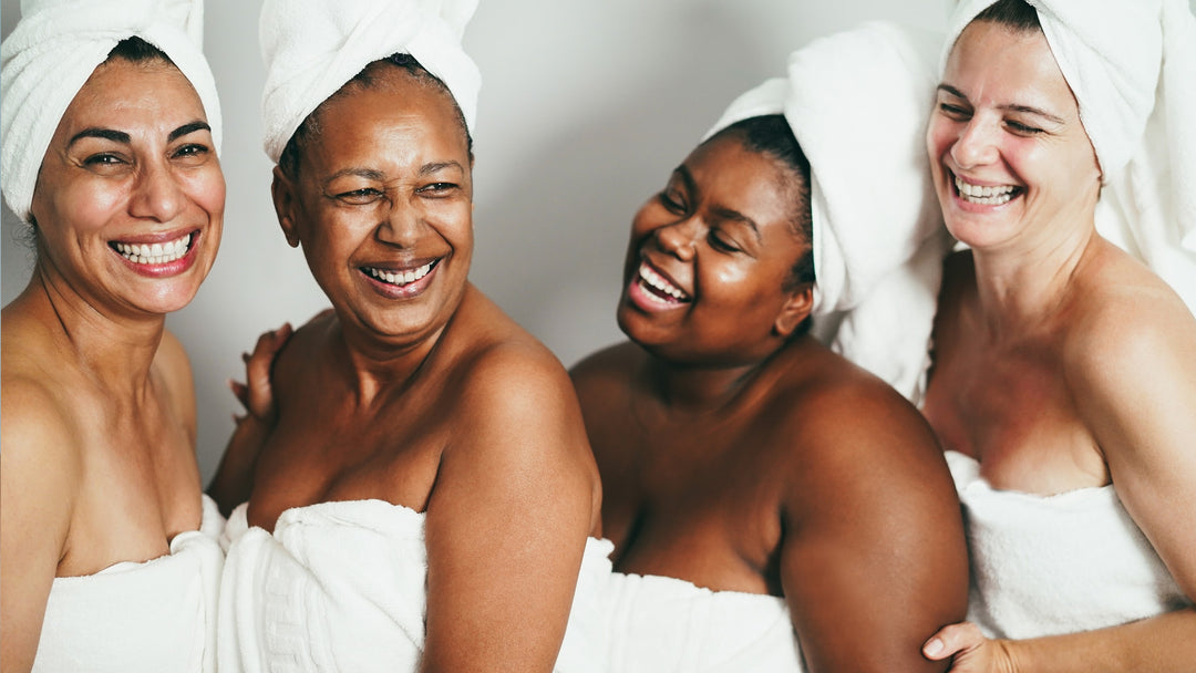 FOUR WOMEN, YOUNG, MIDDLE AGED AND OLDER, OF A VARIETY OF SKINTONES IN WHITE TOWELS, LAUGHING