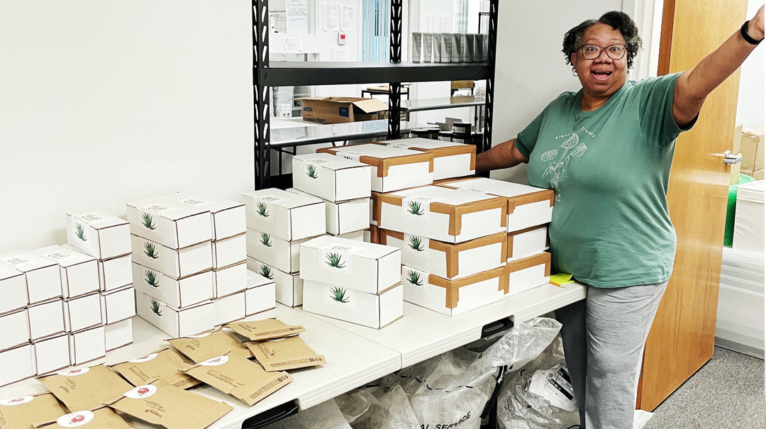 table filled with various sizes of packages and black woman standing nearby with a victorious stance