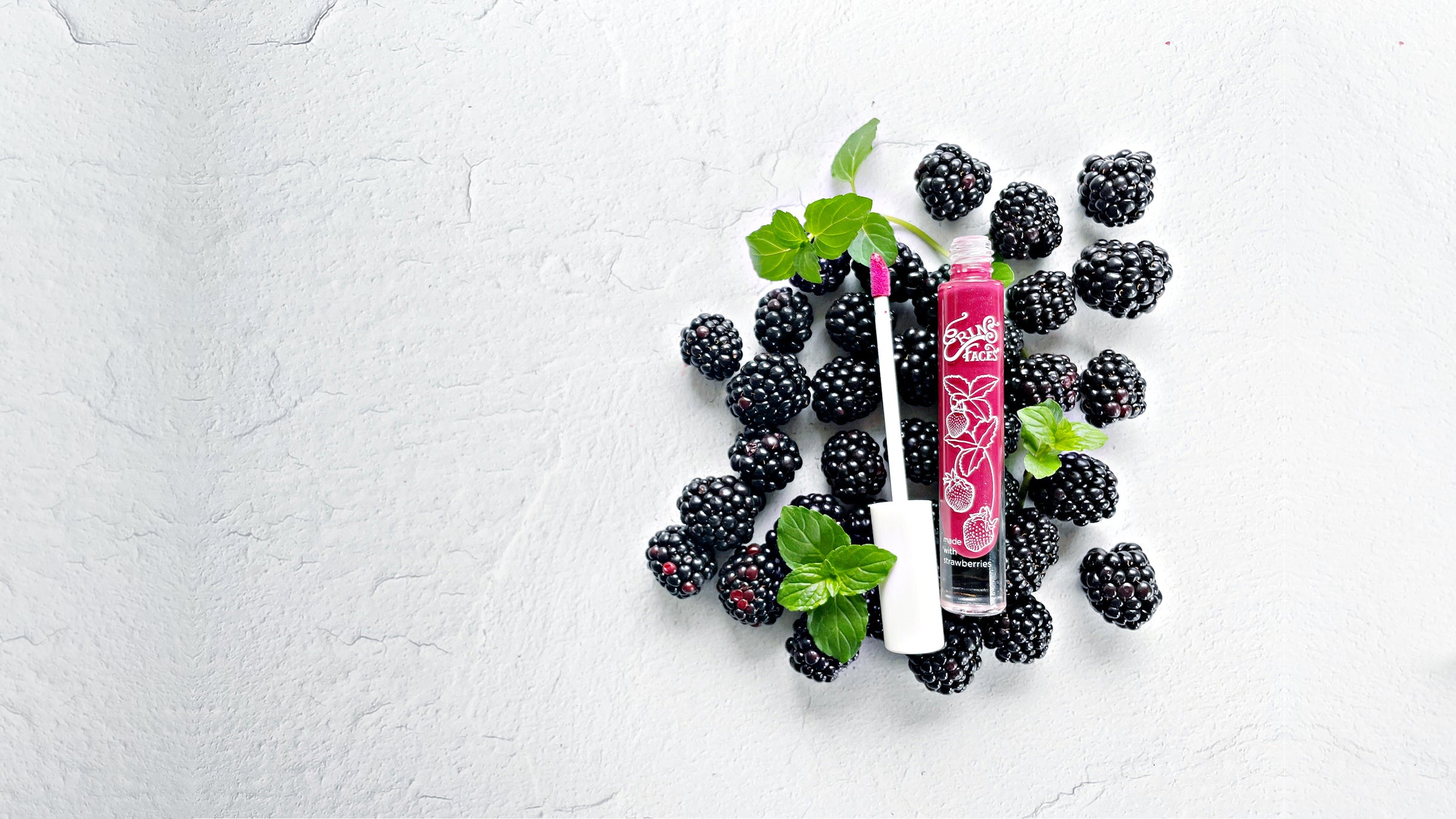 white background with blackberries and mint leaves alongside erin's faces fruit smoothie lip gloss in starbright - a deep pink shade