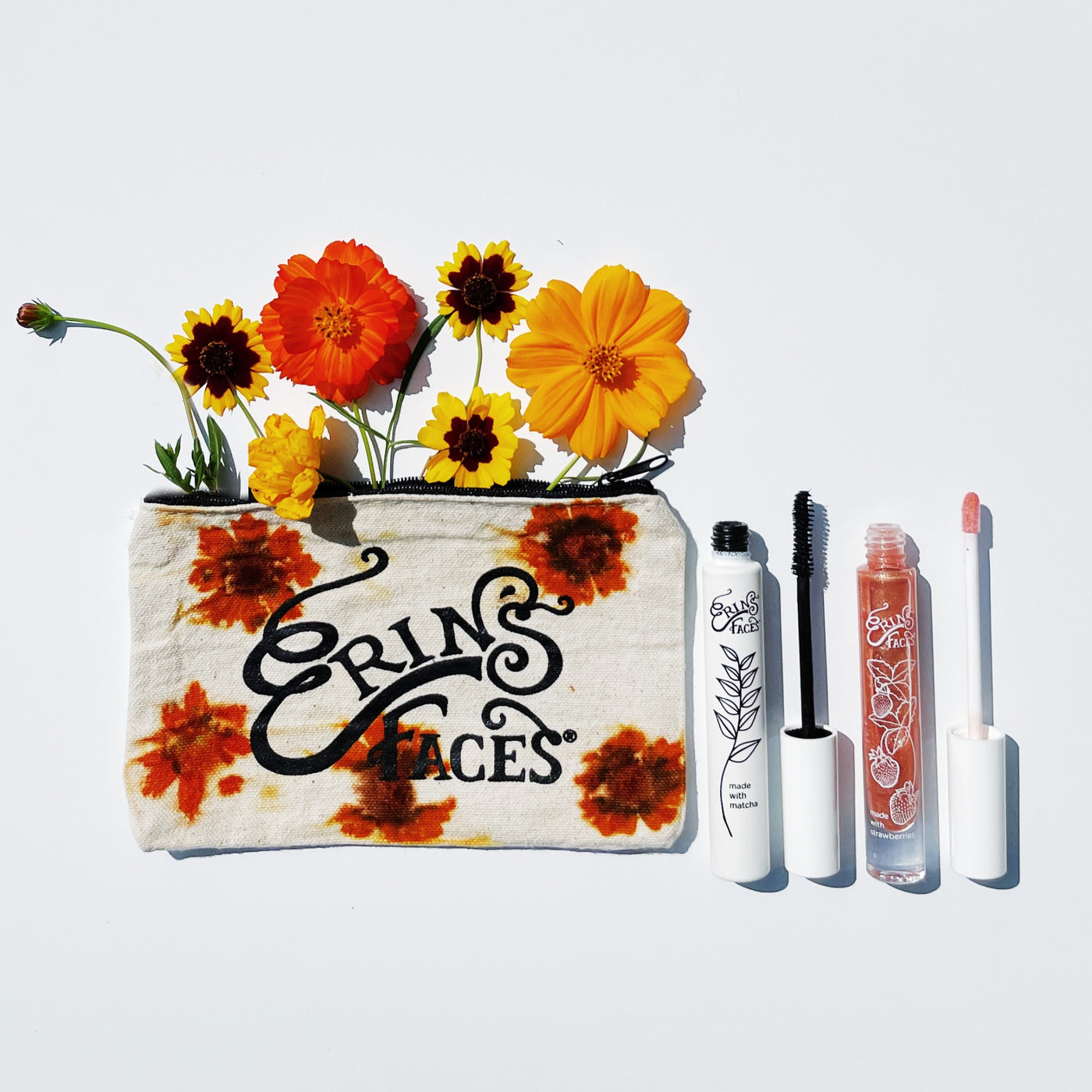 mascara and lip gloss with erin's faces logo bag dyed with yellow flowers with flowers coming out of bag