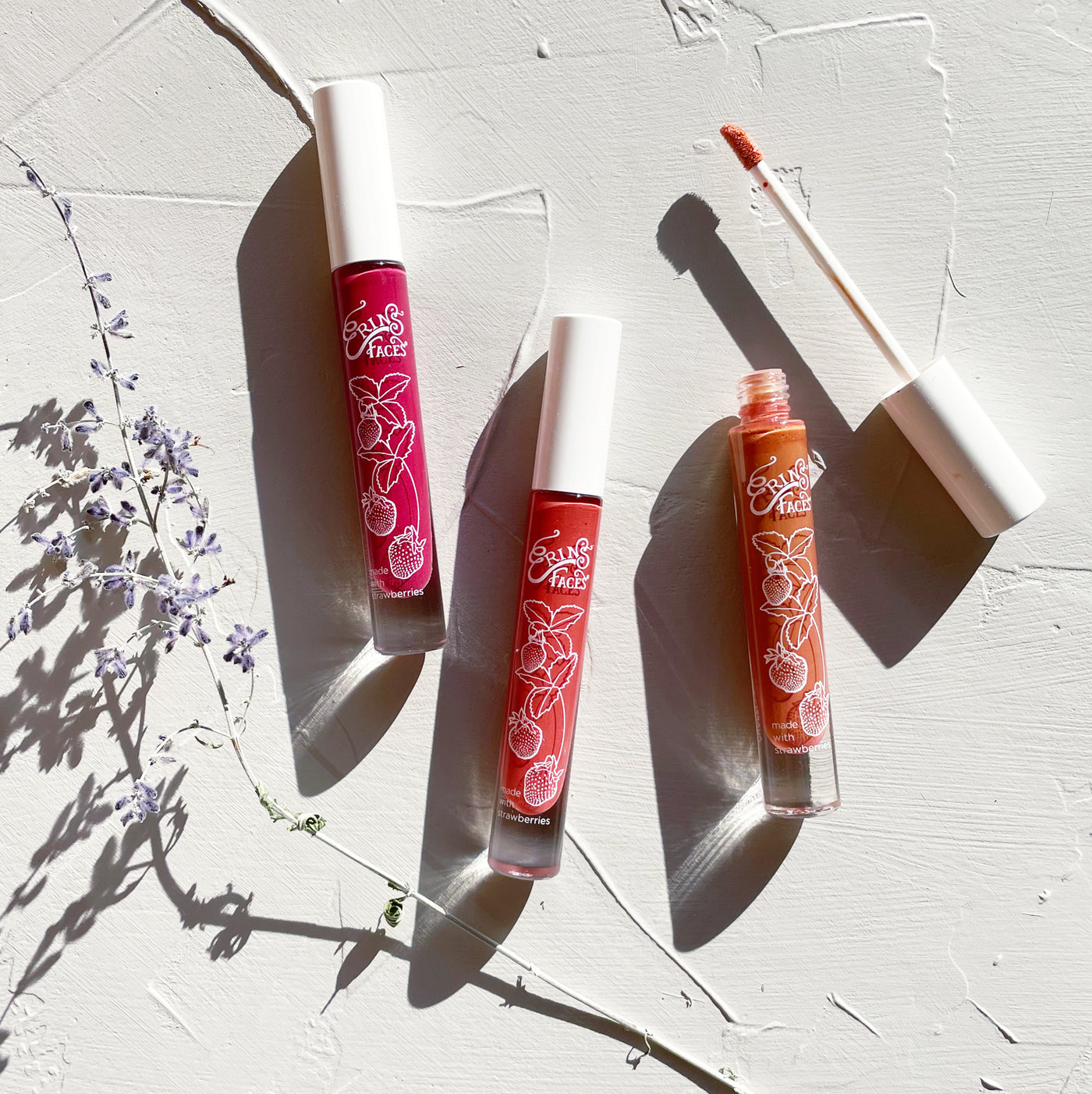 three lip glosses with russian sage on white background