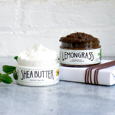 the lemongrass bamboo body scrub exfoliator on top of a white paper wrapped present with brown string by the the shea butter body moisturizer container