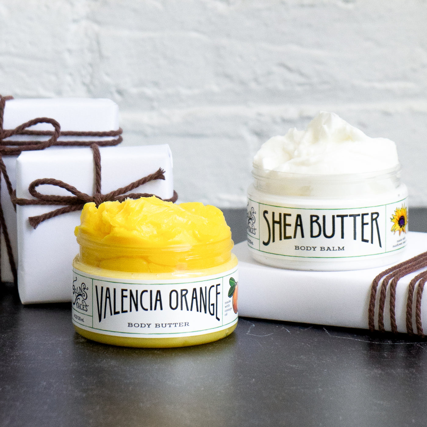 valencia orange and shea butter body balms next to white presents with brown string