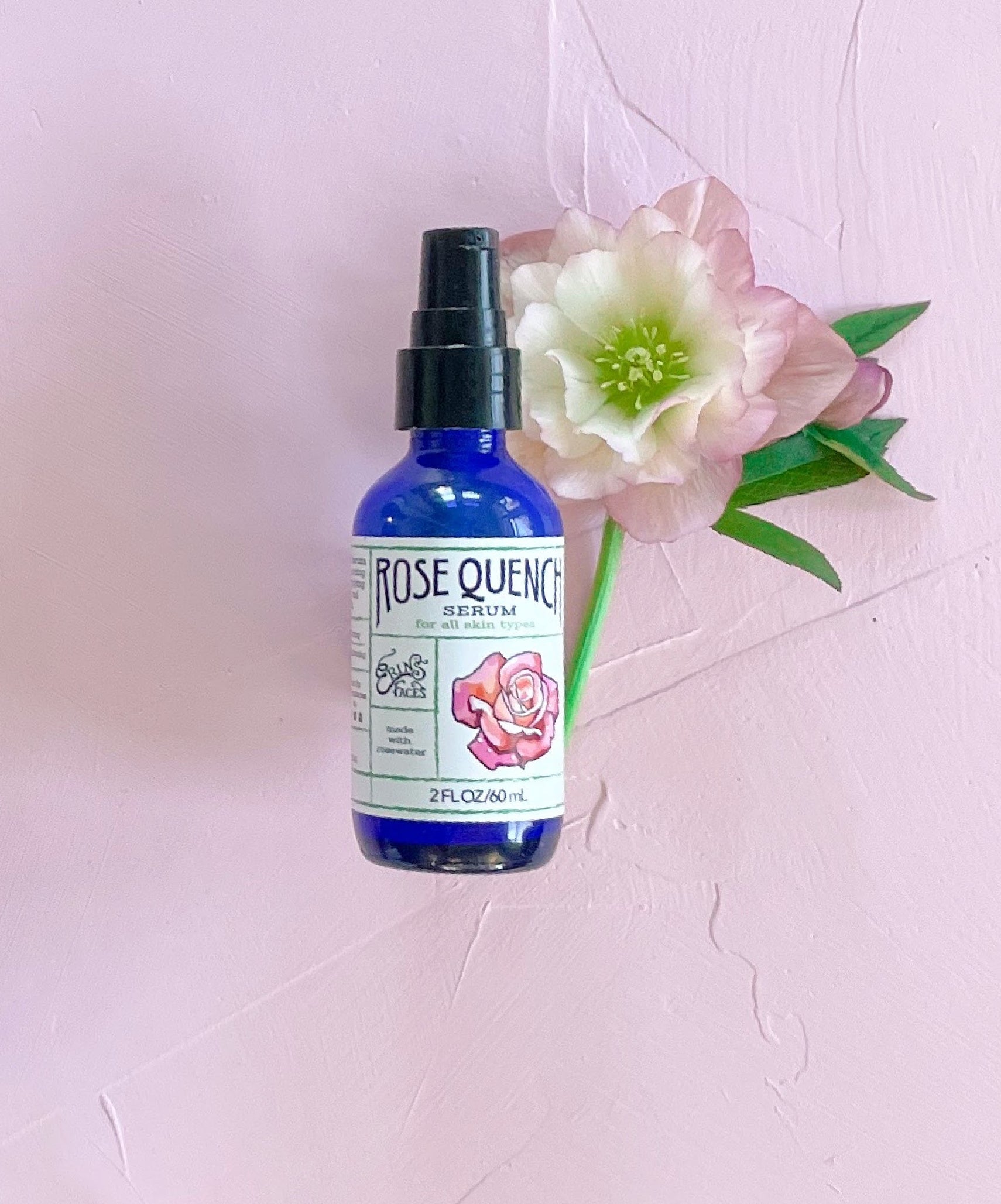 rose quench serum from erin's faces bottle next to white and pink hellebore on pink background